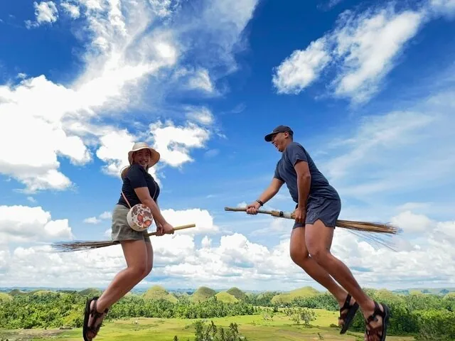Two people jumping on brooms overlooking Chocolate Hills in Bohol
