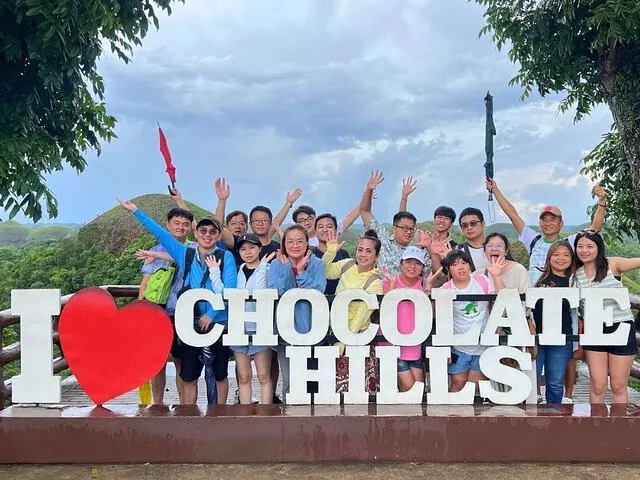 Gruppe von Touristen, die hinter dem Schild 'I Love Chocolate Hills' in Bohol posieren.