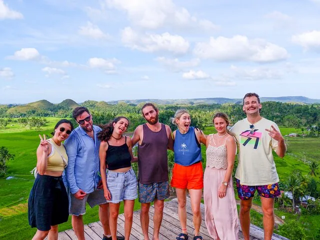 Group of friends posing happily with Chocolate Hills landscape in the background.