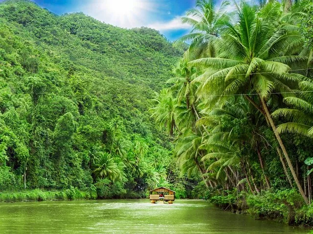 A small raft cruising along a green river surrounded by lush tropical forest.
