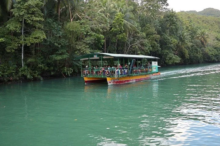 Ein Fahrgastboot auf einem breiten, grünen Fluss, umgeben von dichtem Wald.